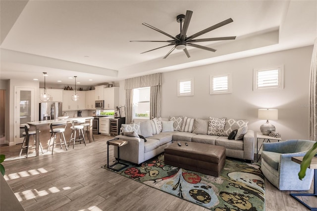 living room featuring light wood-type flooring, a raised ceiling, and ceiling fan