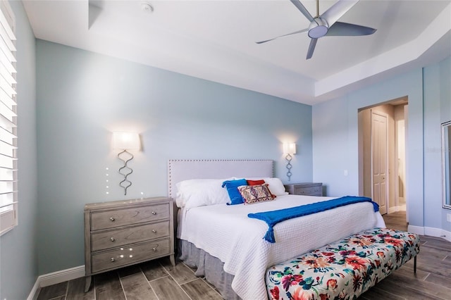 bedroom with ceiling fan, a tray ceiling, wood finish floors, and baseboards