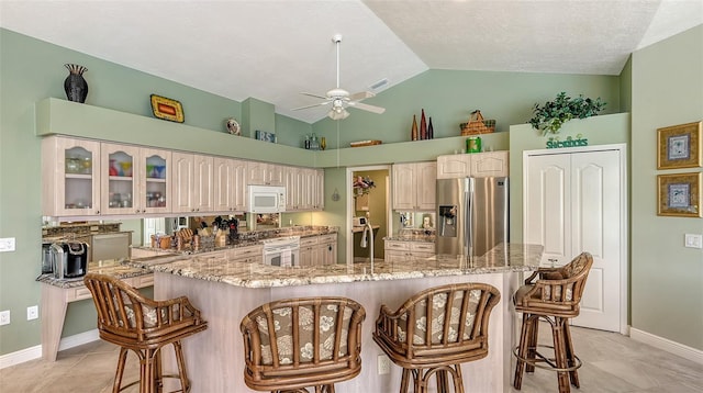 kitchen featuring a ceiling fan, white microwave, a breakfast bar area, and stainless steel fridge with ice dispenser