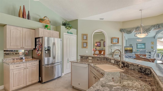 kitchen featuring light stone countertops, lofted ceiling, stainless steel fridge with ice dispenser, a sink, and dishwasher