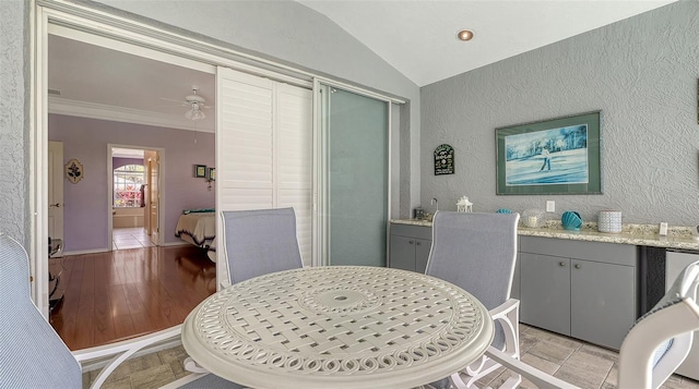 dining room with ornamental molding, a ceiling fan, light wood-style floors, lofted ceiling, and a textured wall