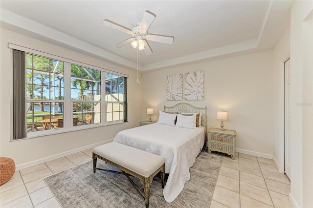 bedroom featuring light tile patterned floors, a tray ceiling, baseboards, and a ceiling fan