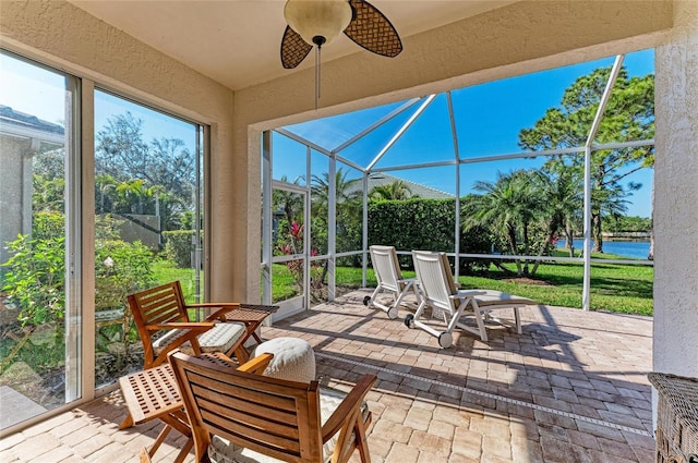 sunroom with ceiling fan and a water view