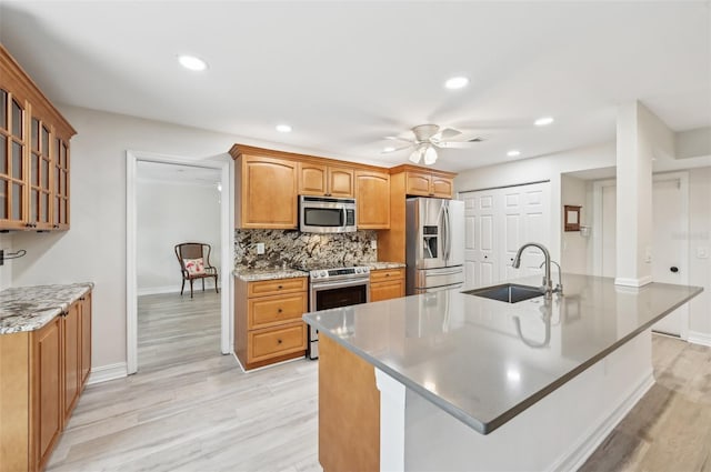 kitchen featuring stainless steel appliances, a sink, a ceiling fan, light wood-type flooring, and decorative backsplash