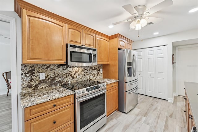 kitchen with light stone countertops, light wood-style flooring, stainless steel appliances, and backsplash