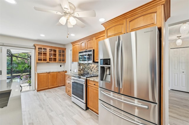 kitchen featuring stainless steel appliances, light wood finished floors, glass insert cabinets, and decorative backsplash