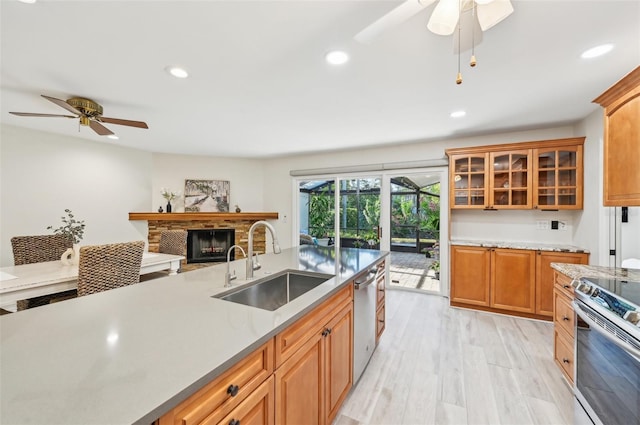 kitchen with electric stove, a sink, light wood-style floors, a fireplace, and stainless steel dishwasher