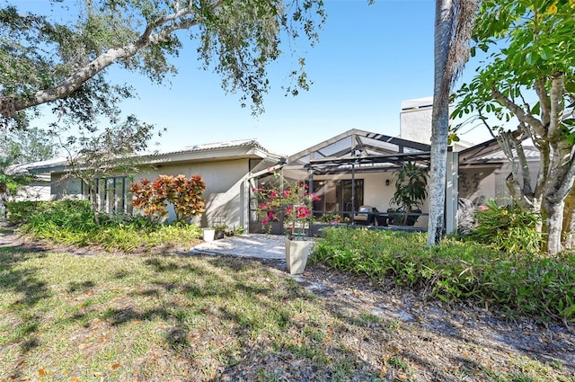 view of front of home with glass enclosure, a chimney, a patio, and stucco siding