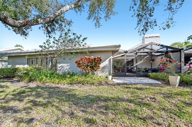 rear view of house with a chimney, a lanai, a yard, a patio area, and stucco siding