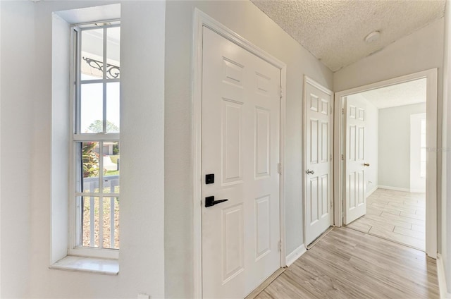 foyer with lofted ceiling, baseboards, a textured ceiling, and light wood finished floors