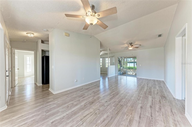 spare room with a textured ceiling, light wood finished floors, lofted ceiling, and visible vents