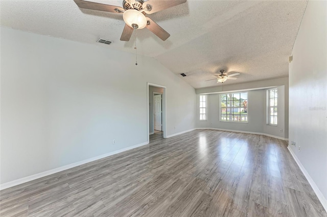 empty room with lofted ceiling, a textured ceiling, visible vents, and wood finished floors