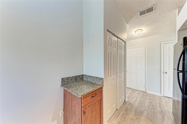 kitchen with brown cabinets, light wood finished floors, visible vents, freestanding refrigerator, and a textured ceiling