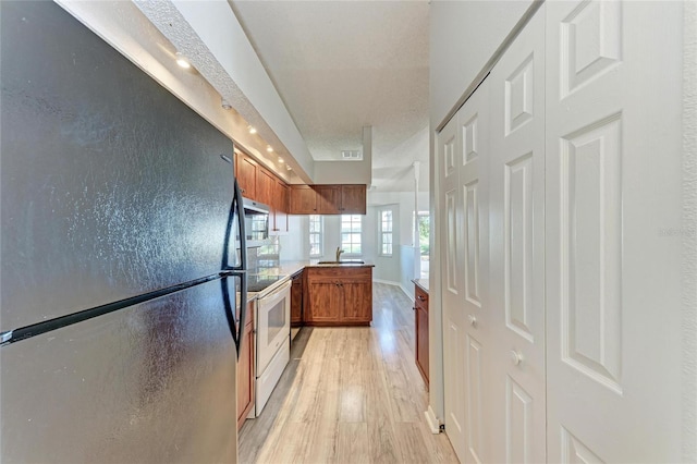 kitchen with visible vents, brown cabinetry, freestanding refrigerator, white electric range, and light wood-type flooring