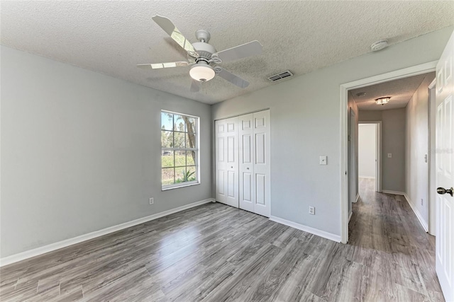 unfurnished bedroom with baseboards, visible vents, wood finished floors, a textured ceiling, and a closet