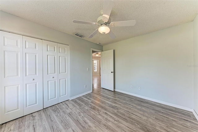 unfurnished bedroom with a textured ceiling, a closet, visible vents, and wood finished floors