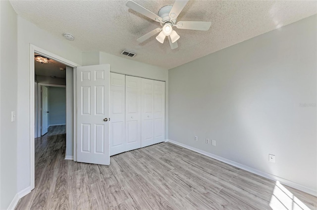 unfurnished bedroom featuring a closet, visible vents, a textured ceiling, and light wood finished floors