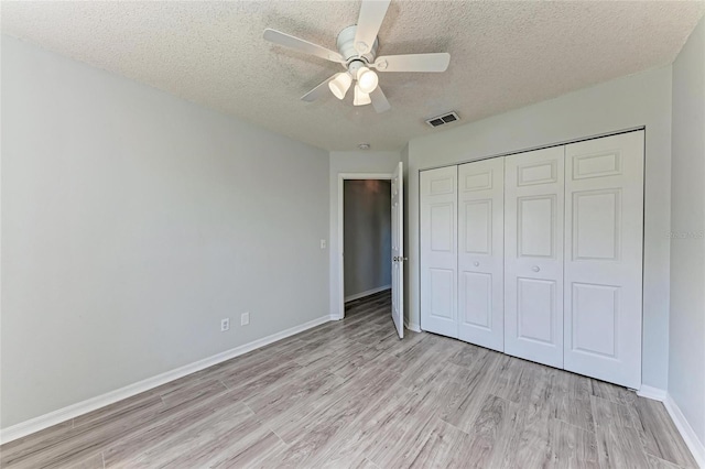 unfurnished bedroom with a textured ceiling, light wood-style flooring, visible vents, baseboards, and a closet