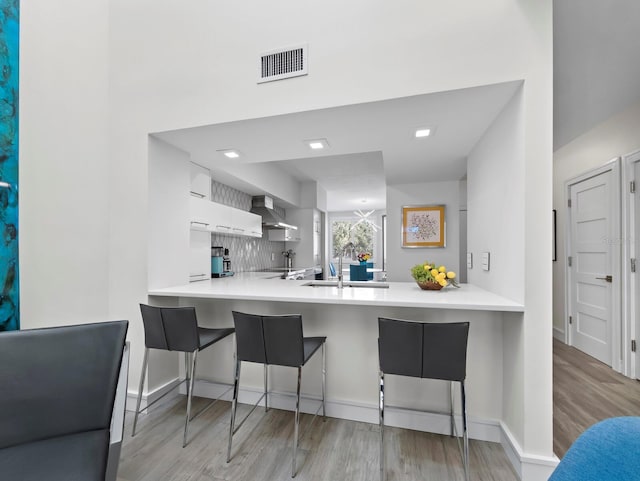 kitchen with visible vents, a peninsula, wall chimney range hood, and a sink