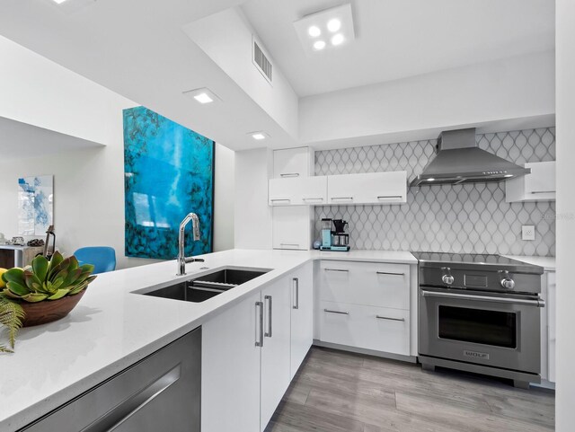 kitchen featuring visible vents, a sink, wall chimney range hood, stainless steel appliances, and modern cabinets