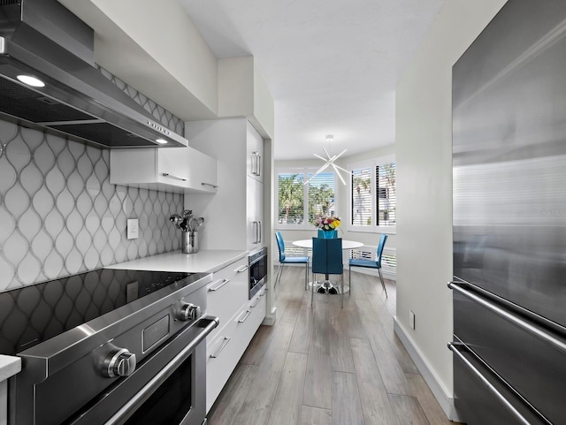 kitchen featuring stainless steel refrigerator, stove, white cabinets, wall chimney exhaust hood, and backsplash