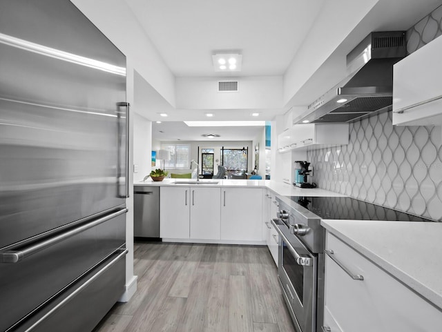 kitchen featuring visible vents, wall chimney range hood, premium appliances, white cabinetry, and a sink