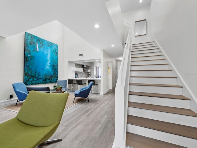 staircase with visible vents, baseboards, recessed lighting, a high ceiling, and wood finished floors