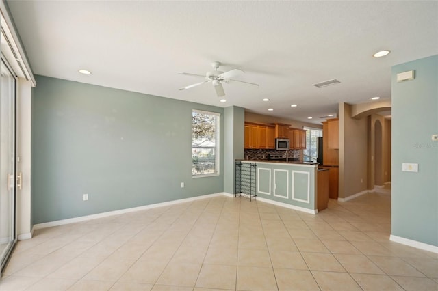 kitchen featuring arched walkways, visible vents, baseboards, decorative backsplash, and stainless steel microwave