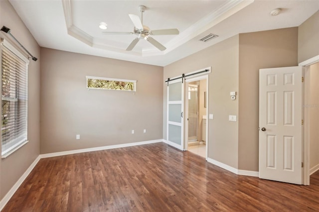 unfurnished bedroom featuring a barn door, wood finished floors, visible vents, baseboards, and a tray ceiling