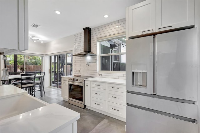 kitchen featuring white cabinets, wall chimney range hood, visible vents, tasteful backsplash, and appliances with stainless steel finishes