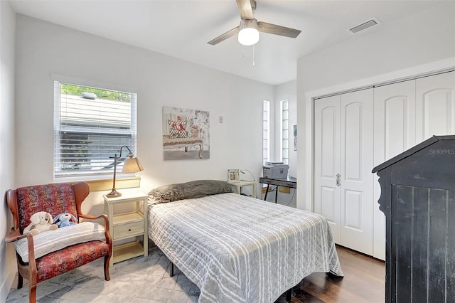 bedroom with a ceiling fan, wood finished floors, visible vents, and a closet