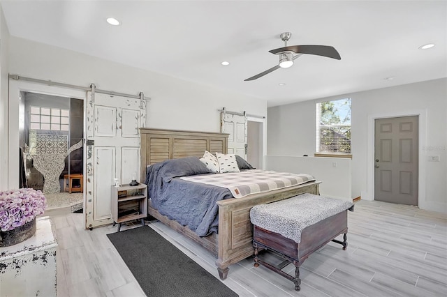 bedroom featuring a barn door, recessed lighting, a ceiling fan, and light wood-style flooring