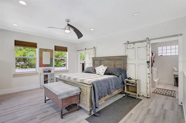 bedroom with light wood-style flooring, baseboards, recessed lighting, and a barn door