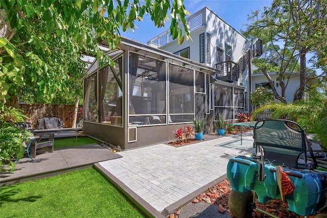 rear view of house with fence, a patio area, a deck, a sunroom, and stucco siding