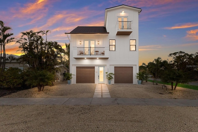 view of front of property featuring french doors, metal roof, driveway, a balcony, and an attached garage