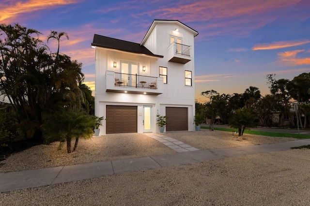 view of front facade featuring a garage, a balcony, gravel driveway, and french doors