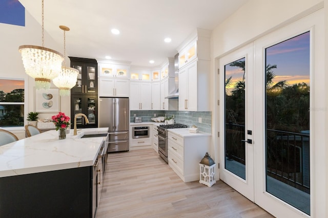 kitchen with high end appliances, light wood finished floors, a sink, decorative backsplash, and french doors