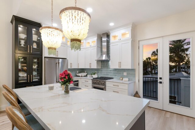 kitchen featuring premium appliances, wall chimney range hood, french doors, light wood finished floors, and decorative backsplash