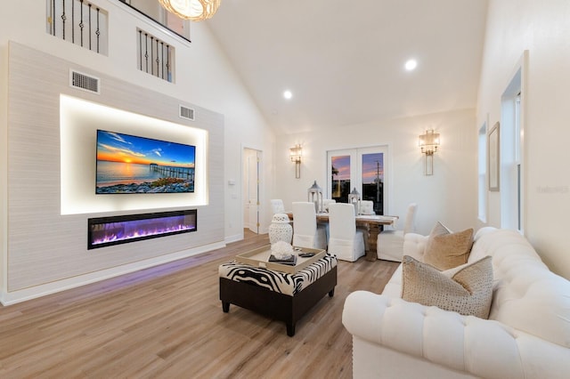 living area with visible vents, high vaulted ceiling, light wood-style floors, and a glass covered fireplace