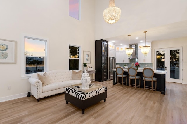 living area featuring baseboards, recessed lighting, a towering ceiling, a notable chandelier, and light wood-type flooring