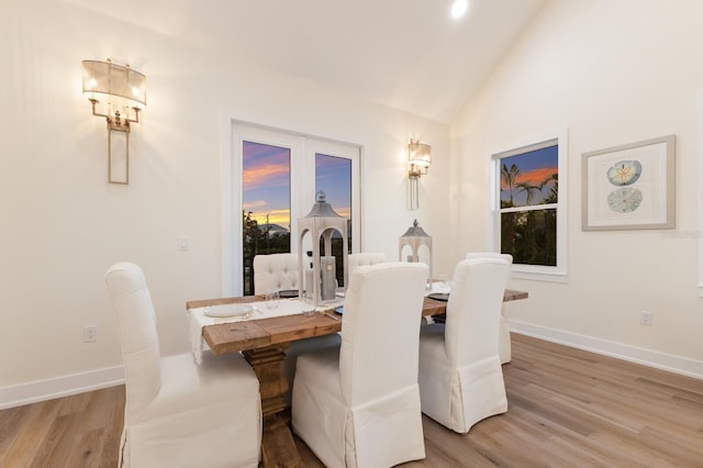 dining area with light wood-style flooring, baseboards, and lofted ceiling