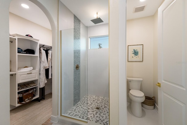 bathroom with visible vents, toilet, a walk in closet, and a stall shower