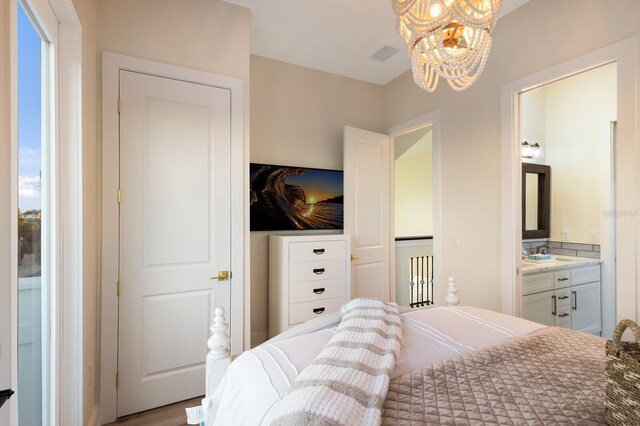 bedroom featuring a notable chandelier, visible vents, connected bathroom, and a sink