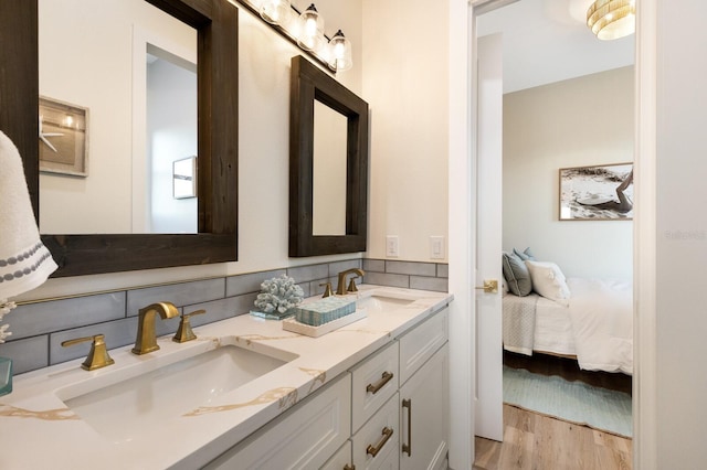 ensuite bathroom featuring ensuite bath, double vanity, wood finished floors, and a sink