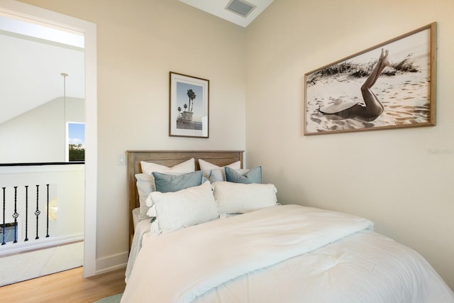 bedroom featuring visible vents, lofted ceiling, baseboards, and wood finished floors