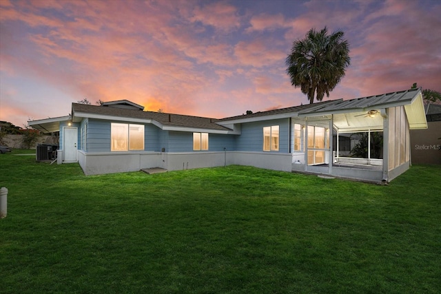 back of house at dusk with cooling unit, a sunroom, and a yard