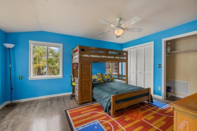 bedroom featuring wood finished floors, visible vents, baseboards, vaulted ceiling, and two closets