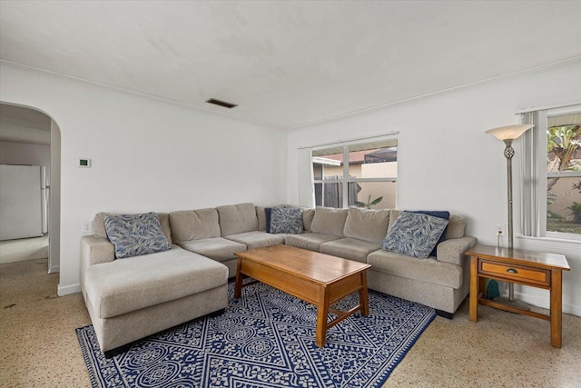 living area featuring plenty of natural light, arched walkways, and speckled floor