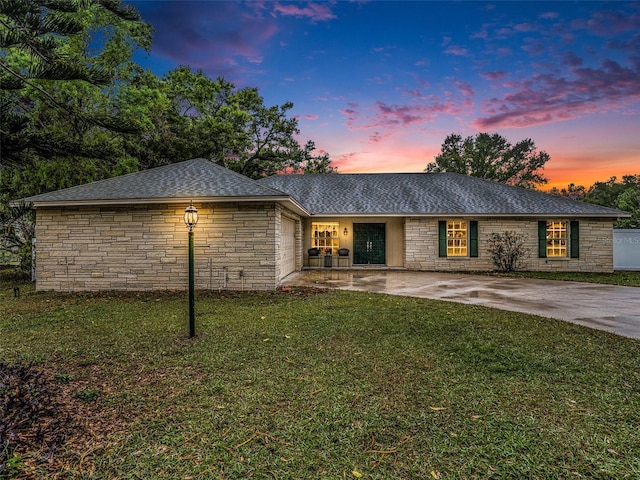 ranch-style home with driveway, stone siding, a front yard, a shingled roof, and a garage