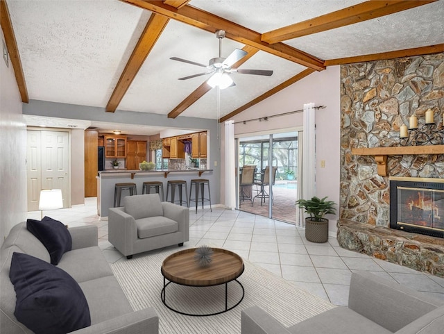 living area with a textured ceiling, vaulted ceiling with beams, light tile patterned flooring, and a fireplace